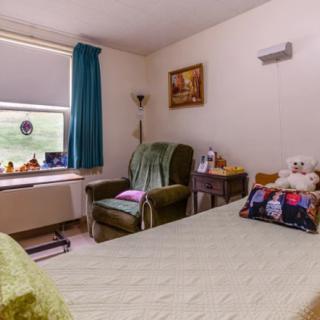 A cozy bedroom with a bed, armchair, and decorative items by the window.