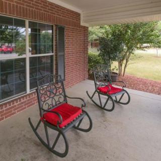 A cozy porch with two rocking chairs featuring red cushions, set against a brick wall and overlooking a garden.