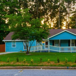 A charming blue house with a porch, surrounded by trees at sunset.