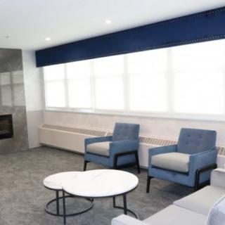 A modern living room with blue chairs, a round coffee table, and large windows.