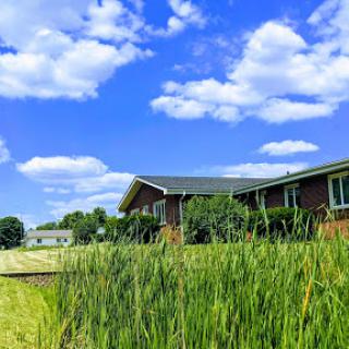 A serene view of a countryside home under a beautiful blue sky dotted with fluffy clouds.