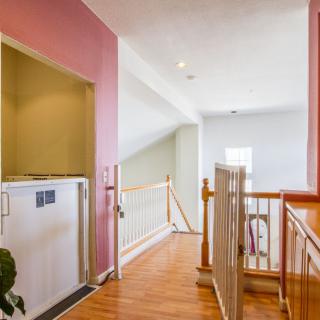 A home hallway featuring a small elevator, wood flooring, and stair railings.