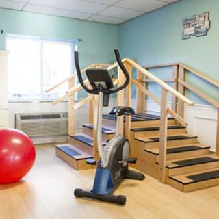 A rehabilitation room featuring a stationary bike, therapy stairs, and a red exercise ball.