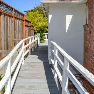 A wooden accessibility ramp with railings leading alongside a house.