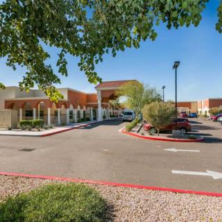 A view of a building entrance with a parking lot and landscaped surroundings on a clear day.