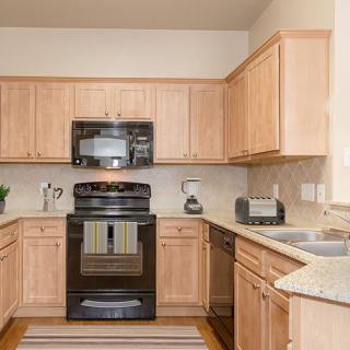 A modern kitchen with light wood cabinets and black appliances.