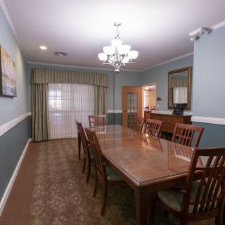 A spacious dining room with a long wooden table, surrounded by chairs and lit by an elegant chandelier.