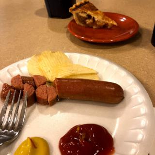 A meal featuring a hot dog with condiments, cheese slices, and a slice of pie in the background.
