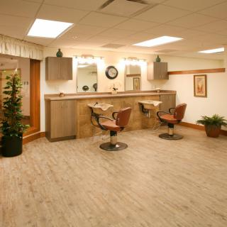 A cozy and well-lit hair salon interior with wooden flooring, comfortable chairs, mirrors, and decorative plants.