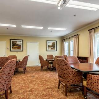 A cozy dining area with multiple tables and upholstered chairs, decorated with paintings and curtains.