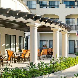 An inviting outdoor patio area with seating under a pergola, adjacent to a building with classic columns and lush landscaping.