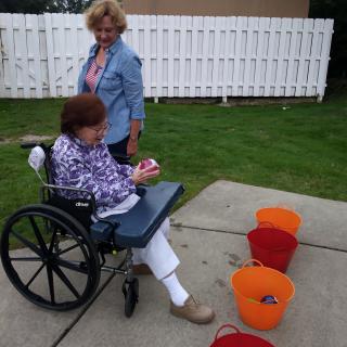 An elderly person in a wheelchair playing a game with buckets outdoors, accompanied by another person.