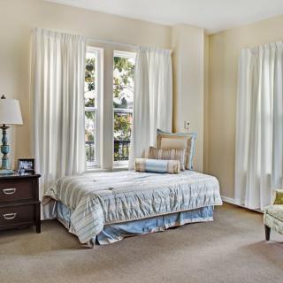 A cozy bedroom with elegant decor, featuring a single bed and large windows with white curtains.