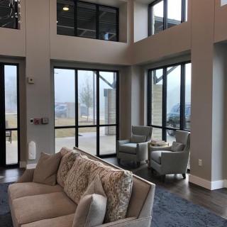 A modern living room with large windows allowing natural light to fill the space, featuring a comfortable sofa and chairs.