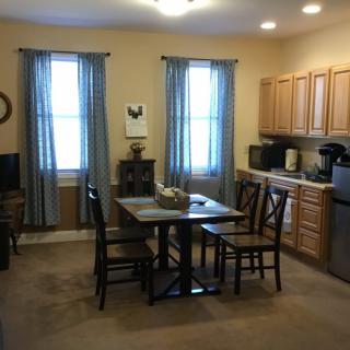 A cozy kitchen with a dining area, featuring wooden cabinets, a small table with four chairs, and blue curtains.