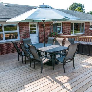 A sunny outdoor deck with patio furniture, including a table, chairs, and an umbrella.