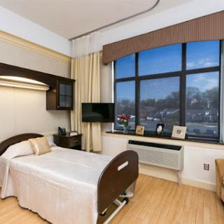A well-lit, modern hospital patient room with a bed, television, and a view outside.