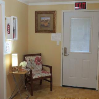 A cozy waiting area with a chair, side table, lamp, and art on the wall near an exit door.