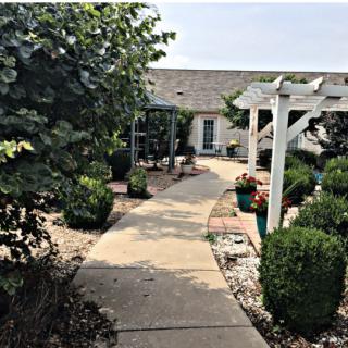 A charming garden pathway leads to a house, featuring lush landscaping and a white pergola.