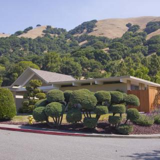 A modern house set against a backdrop of rolling hills and manicured shrubs.