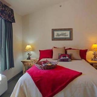 A cozy bedroom with a neatly made bed, adorned with red and beige pillows, flanked by bedside lamps.