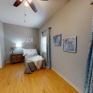 A cozy bedroom with a neatly made bed, nightstand, and lamp, featuring hardwood floors and modern decor.