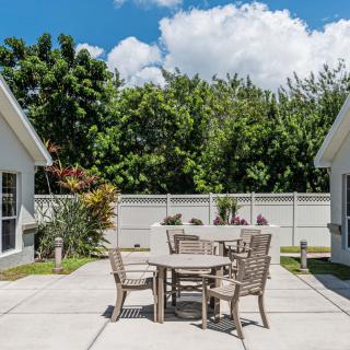 A sunny patio area with a table and chairs, surrounded by trees and a clear blue sky.