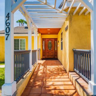 A welcoming entrance to a house with yellow walls and a pergola casting shadows on the pathway.