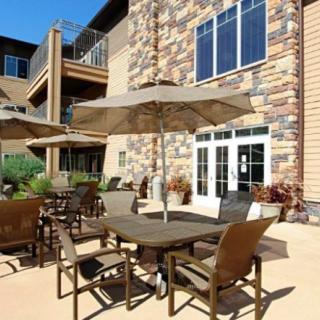 An outdoor patio area with tables, chairs, and umbrellas next to a building with a stone facade.