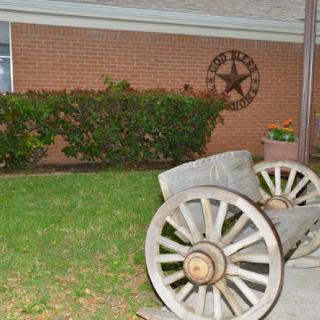 A rustic cannon on display in a garden, with a decorative star on the brick wall behind it.