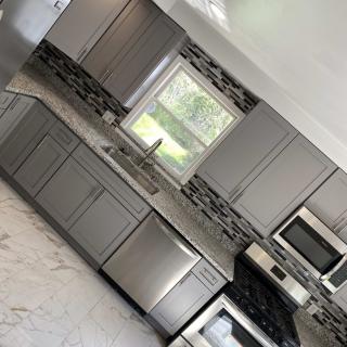 A modern kitchen with gray cabinets, stainless steel appliances, and a marble floor.