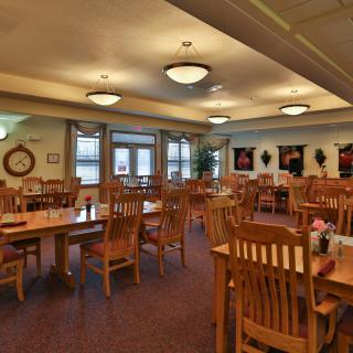 An empty dining room with wooden tables and chairs, warmly lit by ceiling lights.