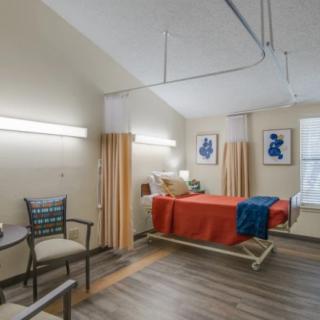 A well-lit hospital room with a single bed, chair, and decorative artwork on the walls.