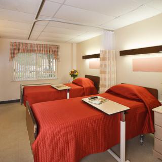 A hospital room with two beds, each equipped with a side table for patient use.
