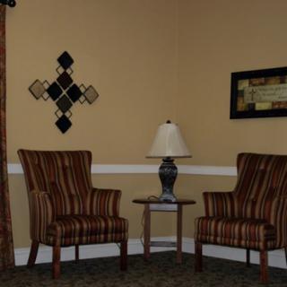 A cozy corner of a living room featuring two striped chairs, a small table with a lamp, and decorative wall art.