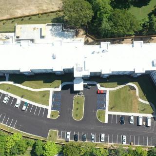 Aerial view of a building with a parking lot and surrounding greenery.