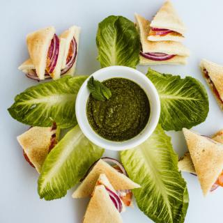 A beautifully arranged platter featuring pita sandwiches with a green dipping sauce, garnished with fresh lettuce leaves.