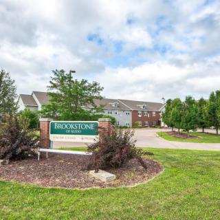 An apartment complex entrance with landscaped greenery and a prominent sign on a cloudy day.