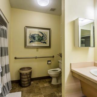A well-lit bathroom featuring a toilet, sink, mirror, and a framed artwork on the wall.