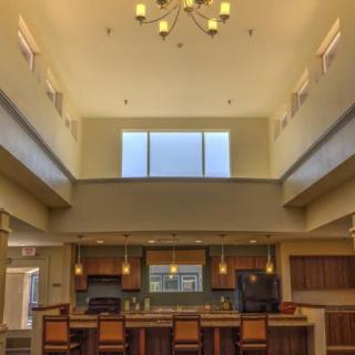 A modern kitchen with an open layout, featuring a high ceiling and a central island under a chandelier.