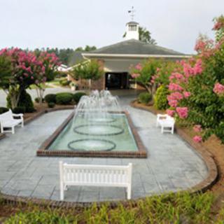 A serene garden setting featuring a central fountain, surrounded by blooming flowers and white benches.