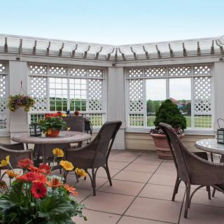 An inviting patio area with comfortable chairs and tables, surrounded by greenery and colorful flowers under a pergola.