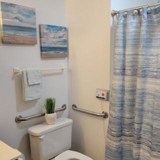 A cozy bathroom featuring beach-themed decor, a colorful shower curtain, and a touch of greenery.