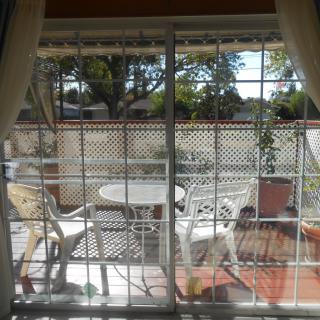 A sunny patio with white furniture viewed through a glass door.