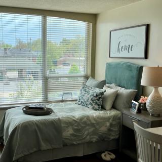 A cozy bedroom with a neatly made bed, large window, and stylish decor.