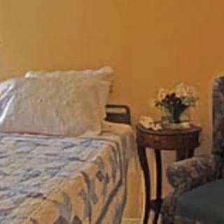 A cozy bedroom corner featuring a bed, a chair, and a small table with a flower vase.