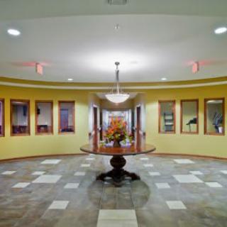 A well-lit lobby with a central table and chandelier, surrounded by yellow walls and tiled flooring.