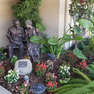 A serene garden featuring a beautiful sculpture of two figures amidst vibrant flowers and lush plants.