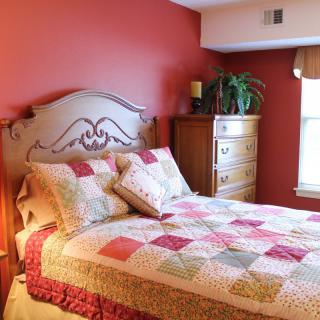 A cozy bedroom with a colorful quilt and red accent wall.