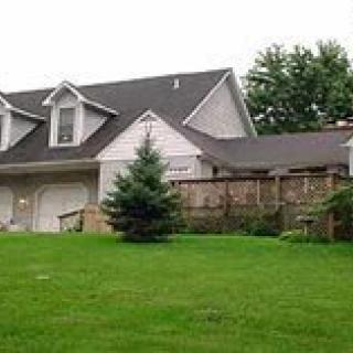 A suburban house with a large green lawn and surrounding trees.